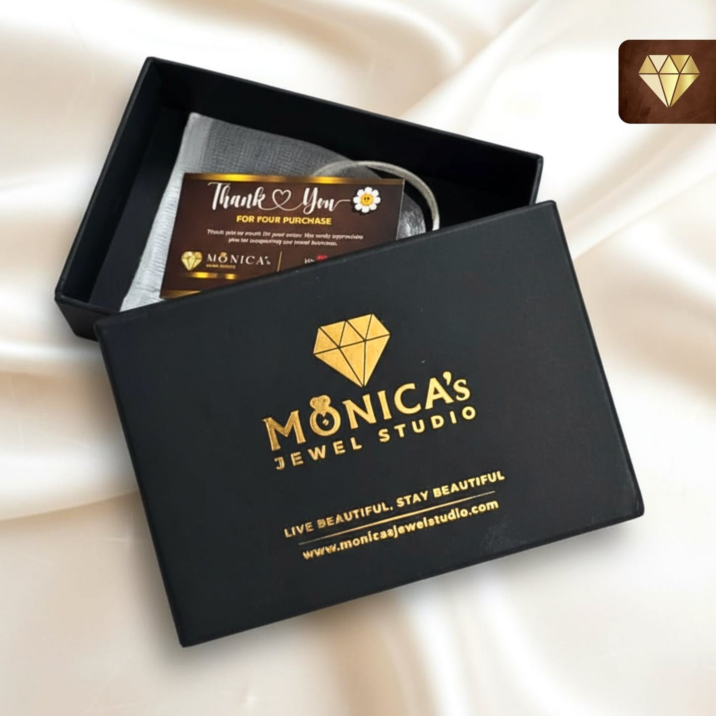 Black jewelry box with 'Monica's Jewel Studio' branding on a beige fabric background