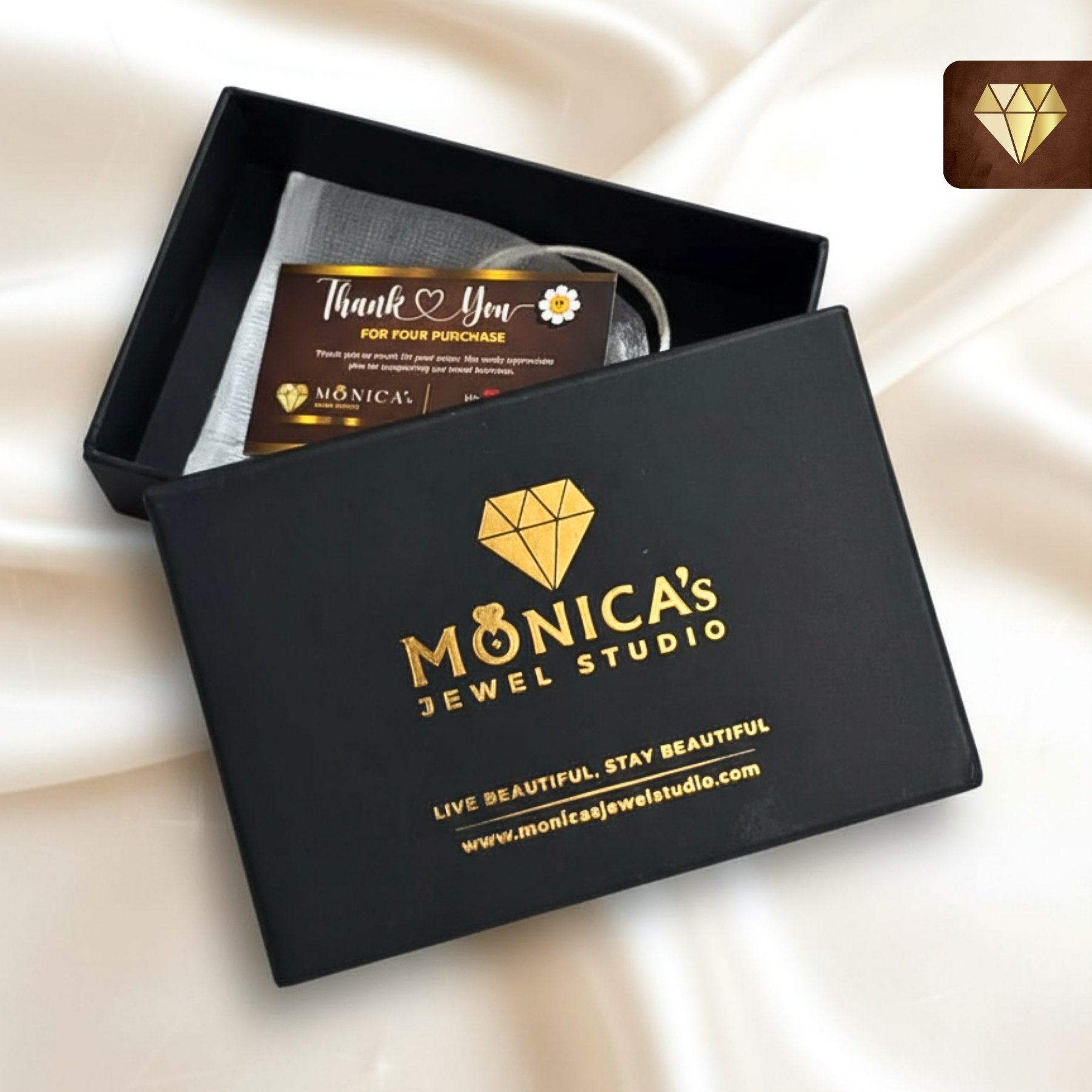 Black jewelry box with 'Monica's Jewel Studio' branding on a beige fabric background